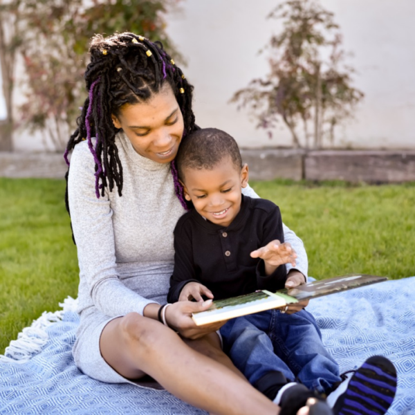 a person and child sitting on a blanket reading a book
